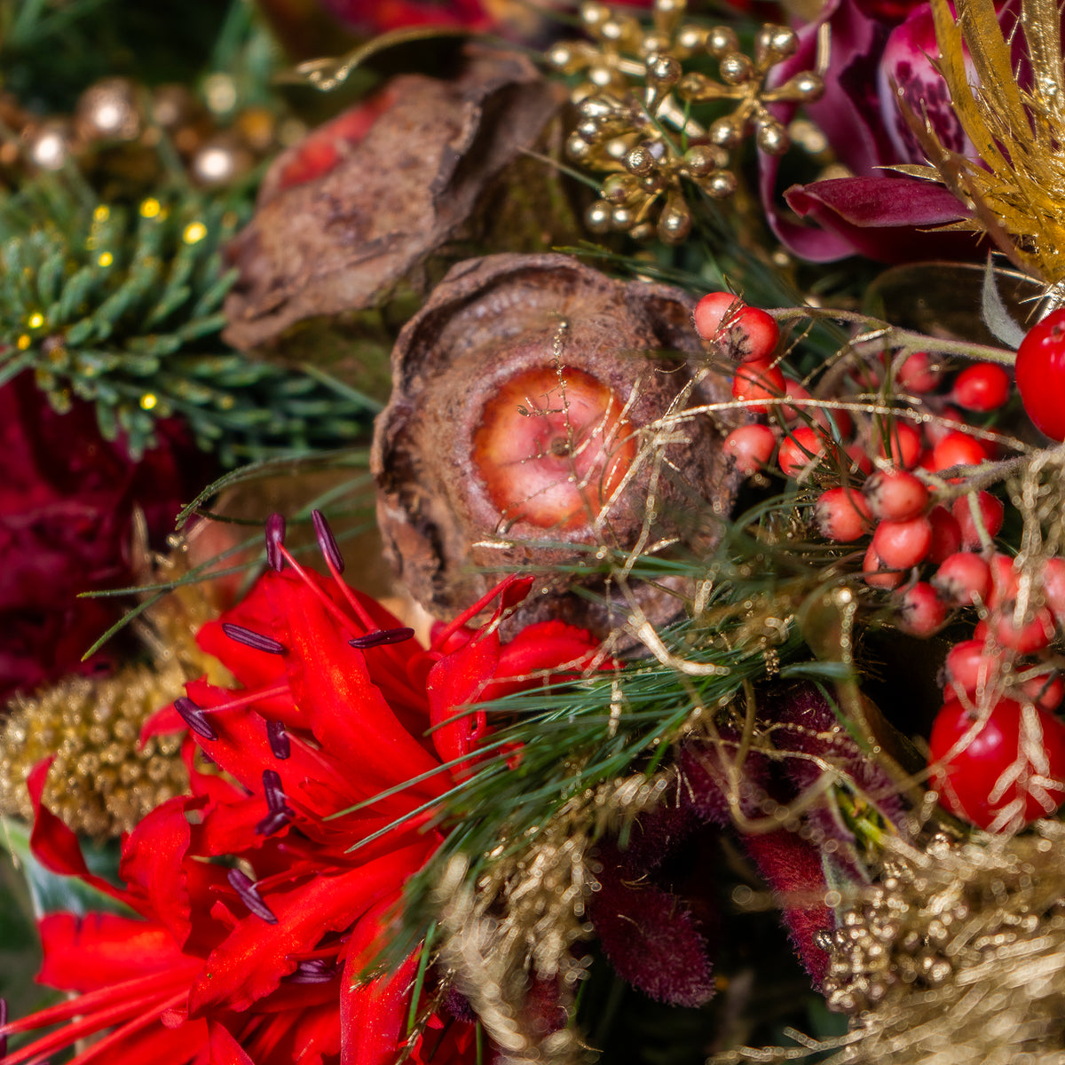 Close-up of a festive floral arrangement with red flowers, berries, and gold accents.