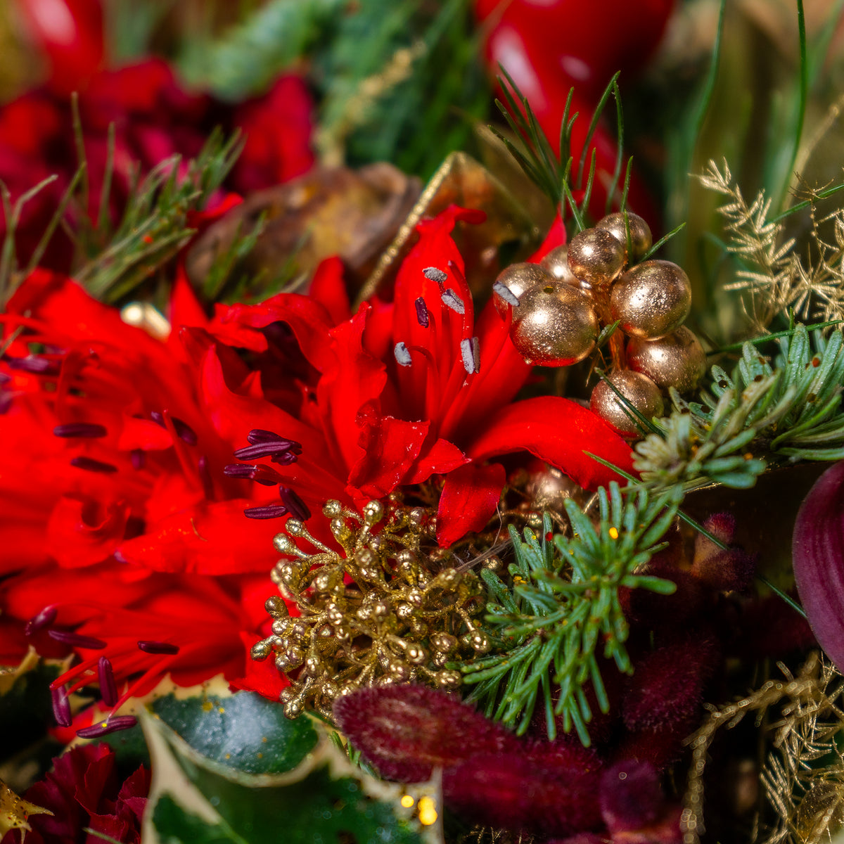 Close-up of a festive flower arrangement with red flowers, gold berries, and greenery.