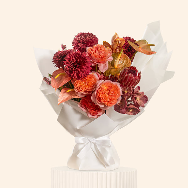 Bouquet of flowers wrapped in white paper with a white ribbon on a light beige background