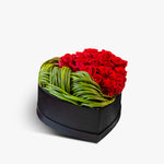 Heart-shaped arrangement of red roses and green leaves in a black box on a white background