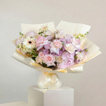 Bouquet of flowers wrapped in paper on a white pedestal against a light gray background