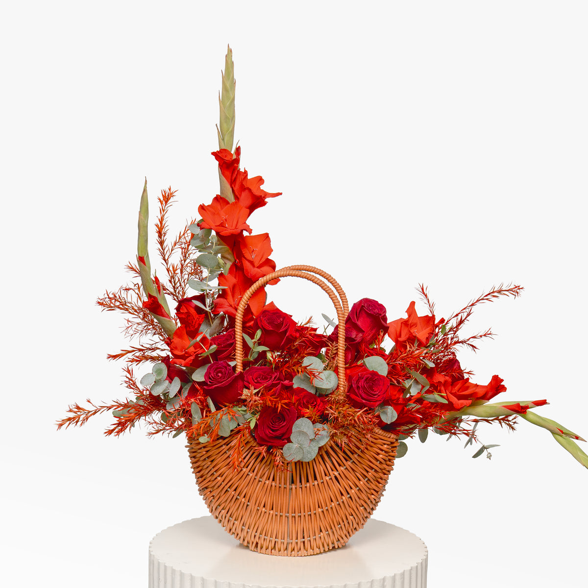 Wicker basket filled with red and orange flowers on a white pedestal