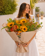 Woman holding a bouquet of sunflowers and other flowers outdoors.