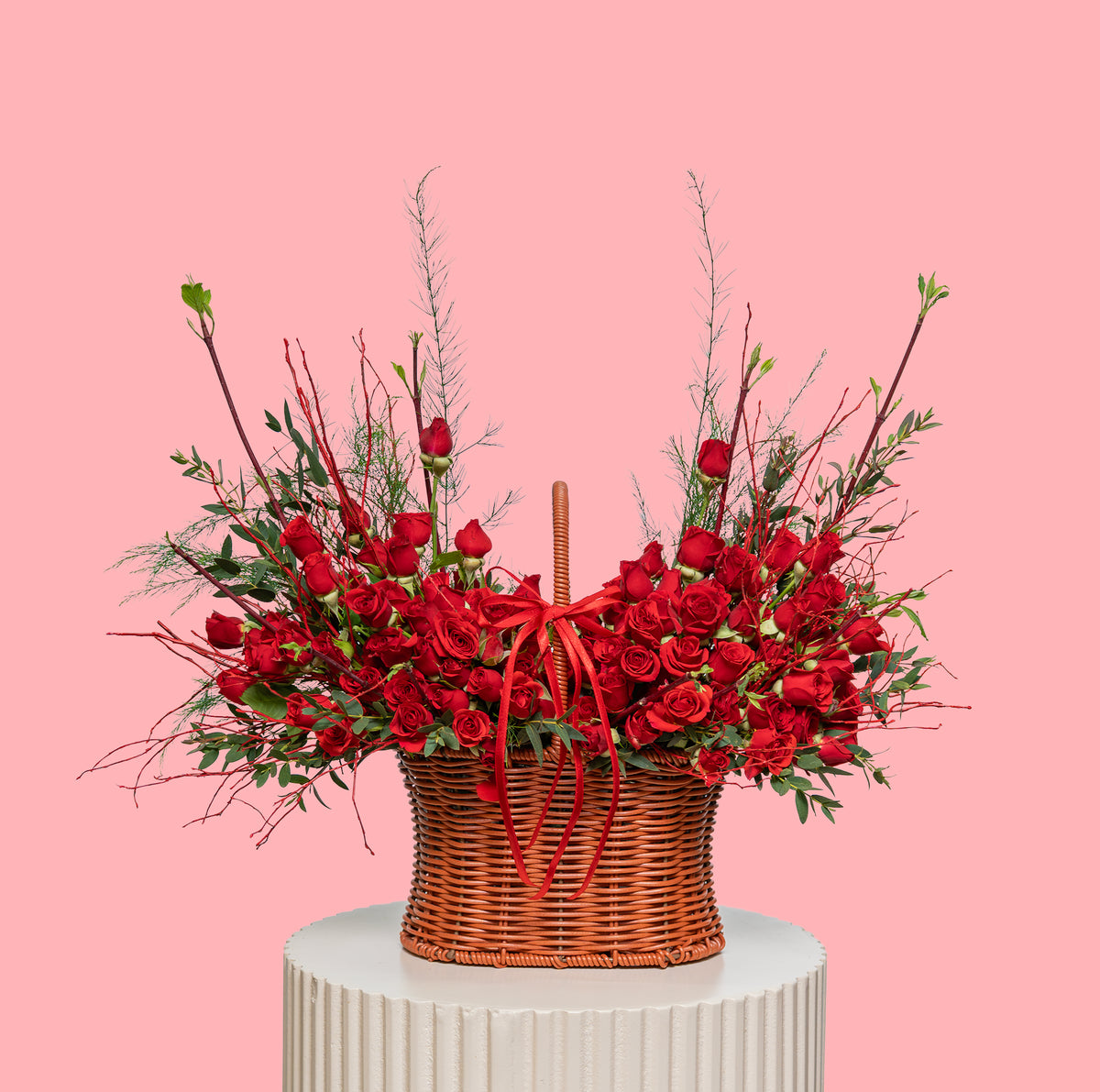 Basket of red roses with greenery on a pink background
