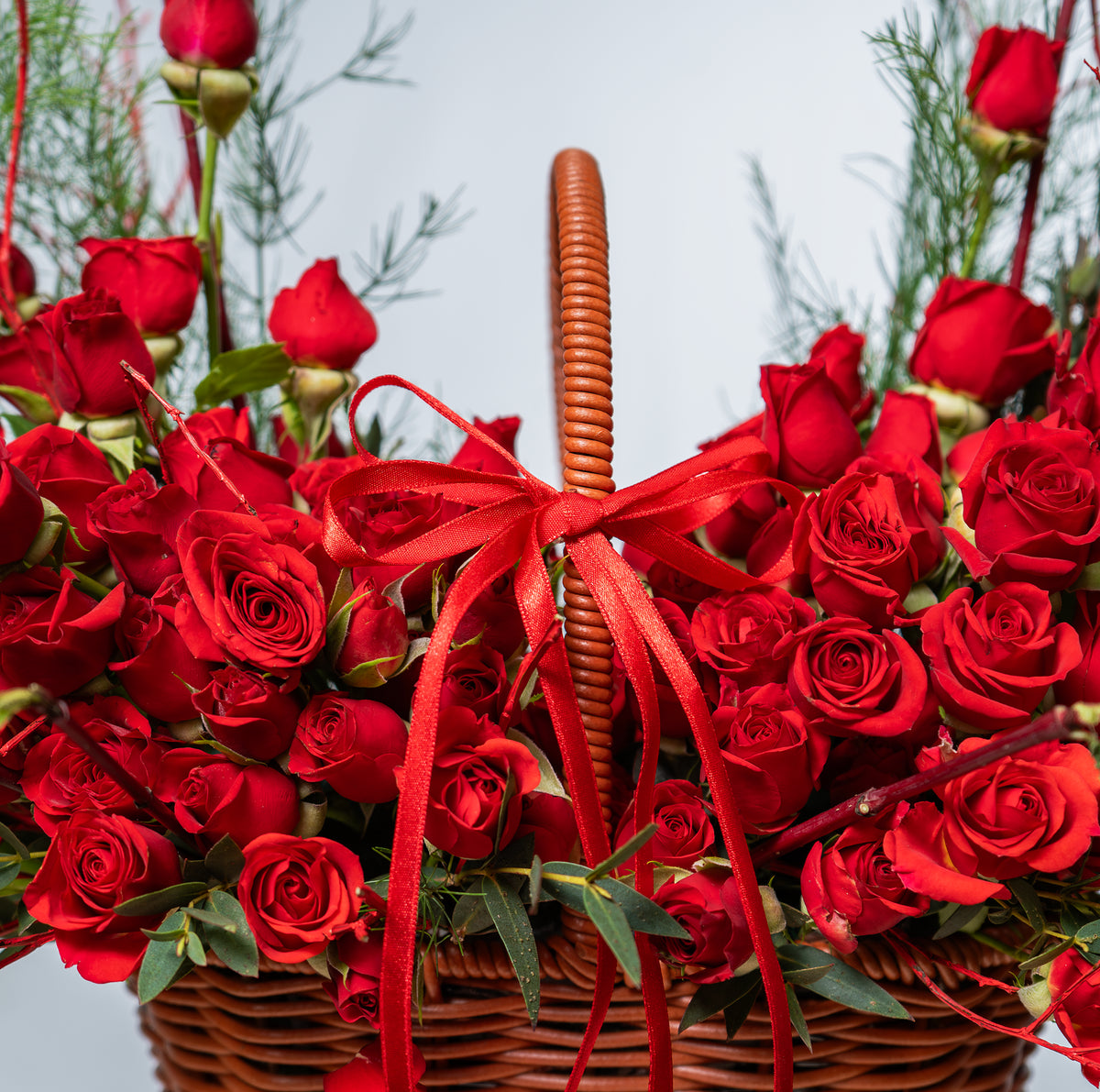 Basket of red roses with a red ribbon against a blurred natural background