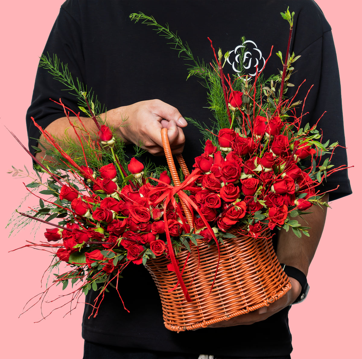 Person holding a basket of red roses against a pink background