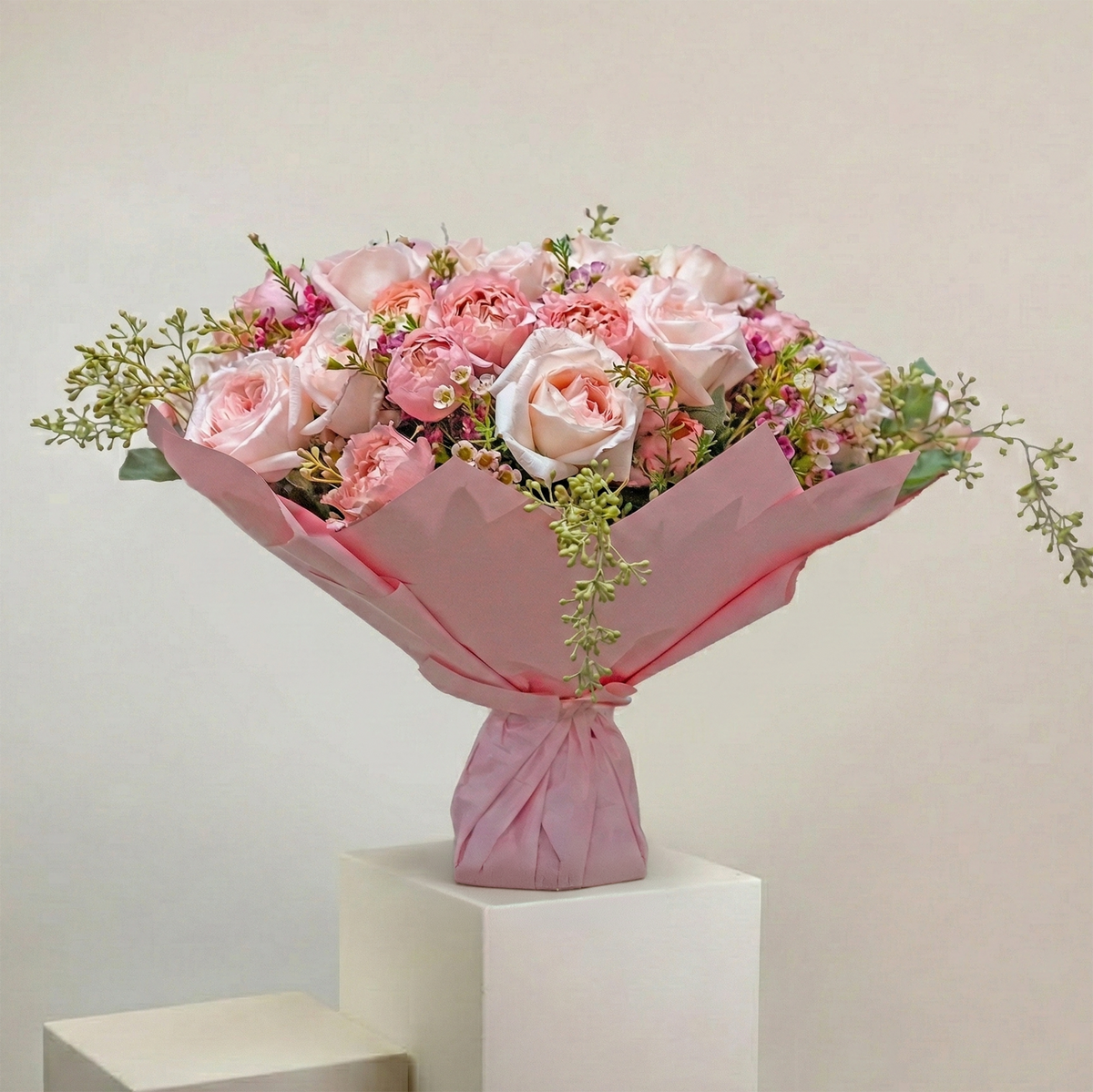 Bouquet of pink roses wrapped in pink paper on a white pedestal against a light beige background