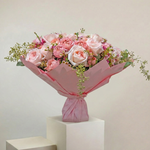 Bouquet of pink roses wrapped in pink paper on a white pedestal against a light beige background