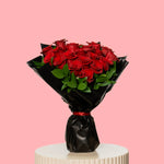 Bouquet of red roses wrapped in black paper on a pink background