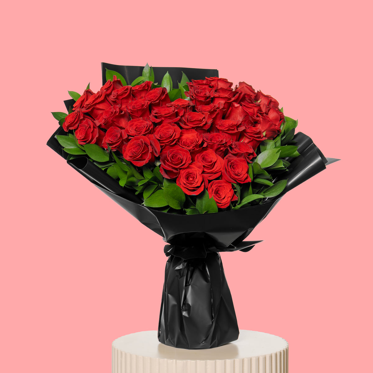 Bouquet of red roses wrapped in black paper on a pink background