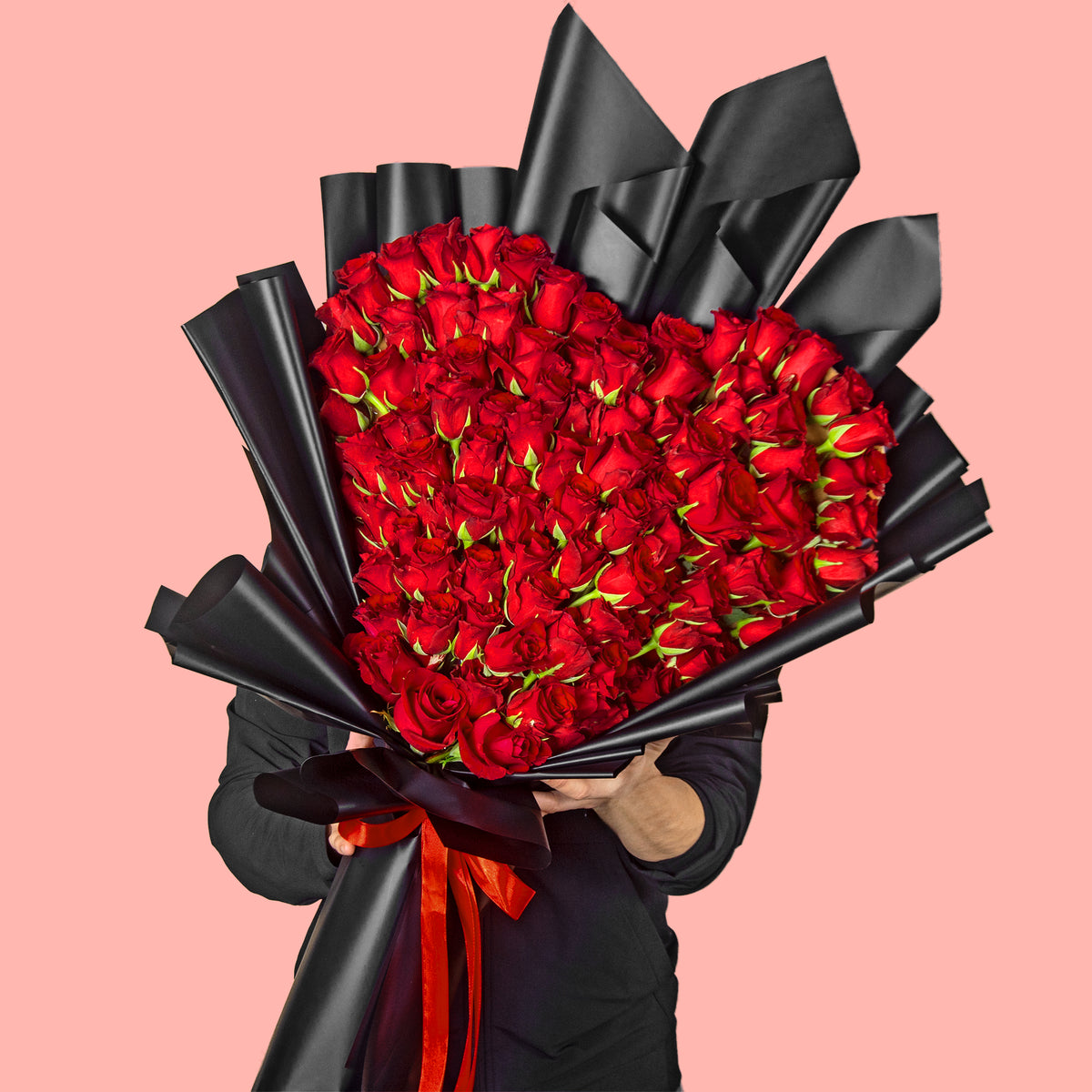 Bouquet of red roses wrapped in black paper and ribbon on a pink background