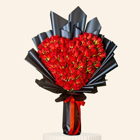 Bouquet of red roses wrapped in black paper and ribbon on a pink background