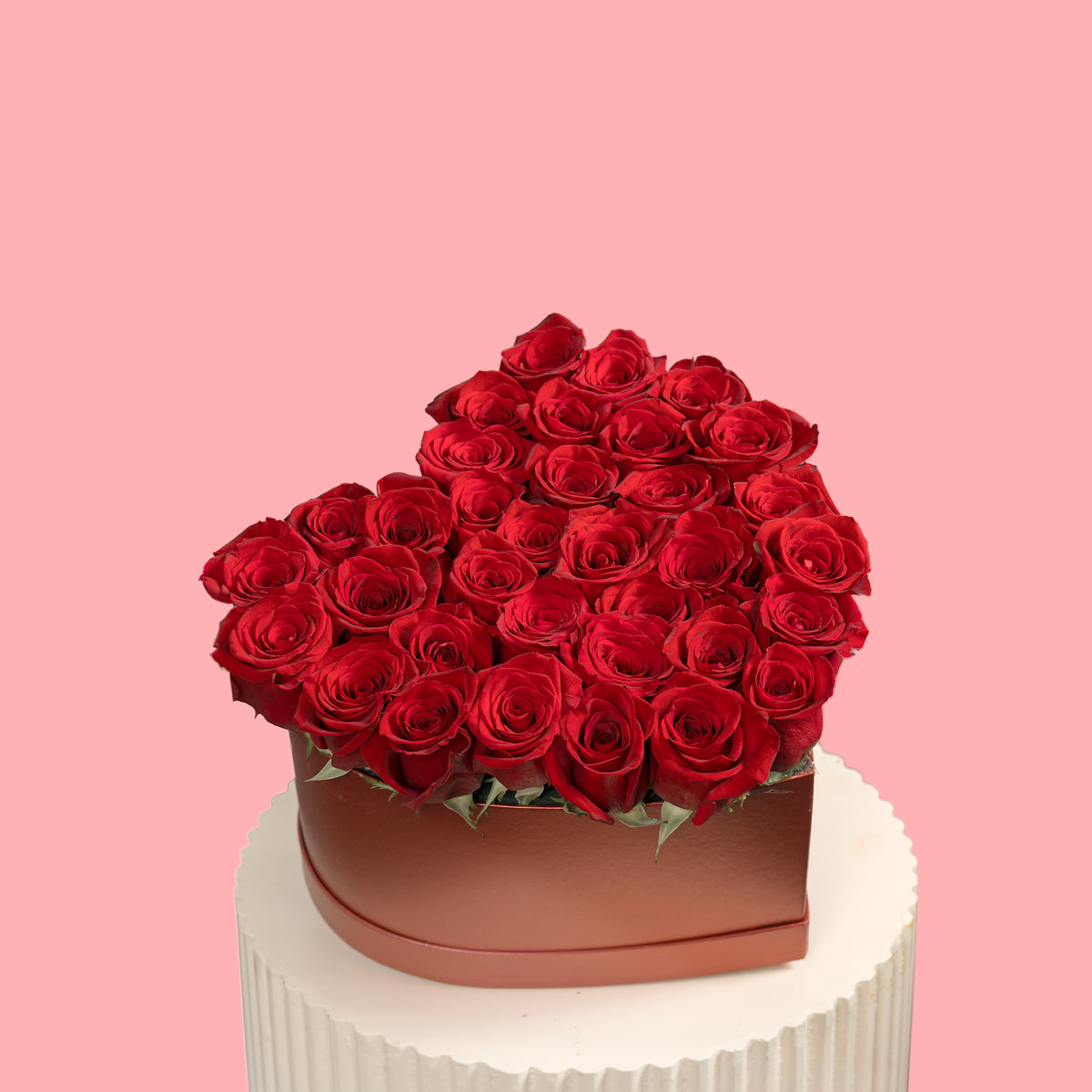Heart-shaped box filled with red roses on a pink background