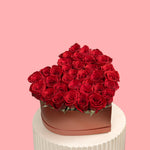 Heart-shaped box filled with red roses on a pink background