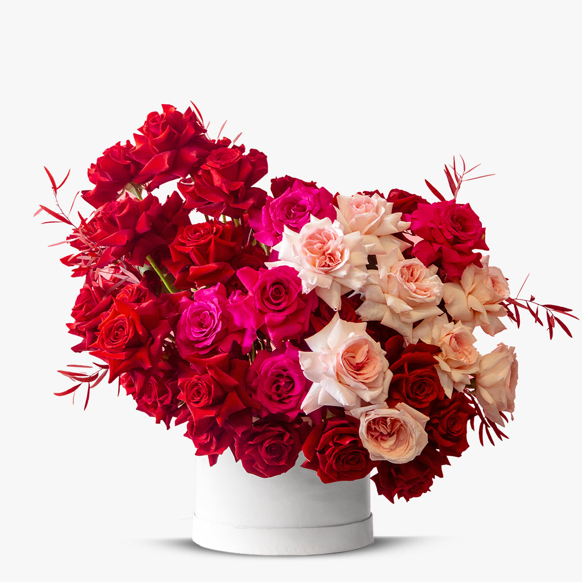 Heart-shaped bouquet of red, pink, and beige roses in a white box on a light gray background