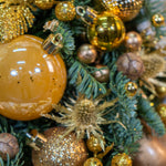 Close-up of Christmas ornaments including gold and brown balls on a green wreath.