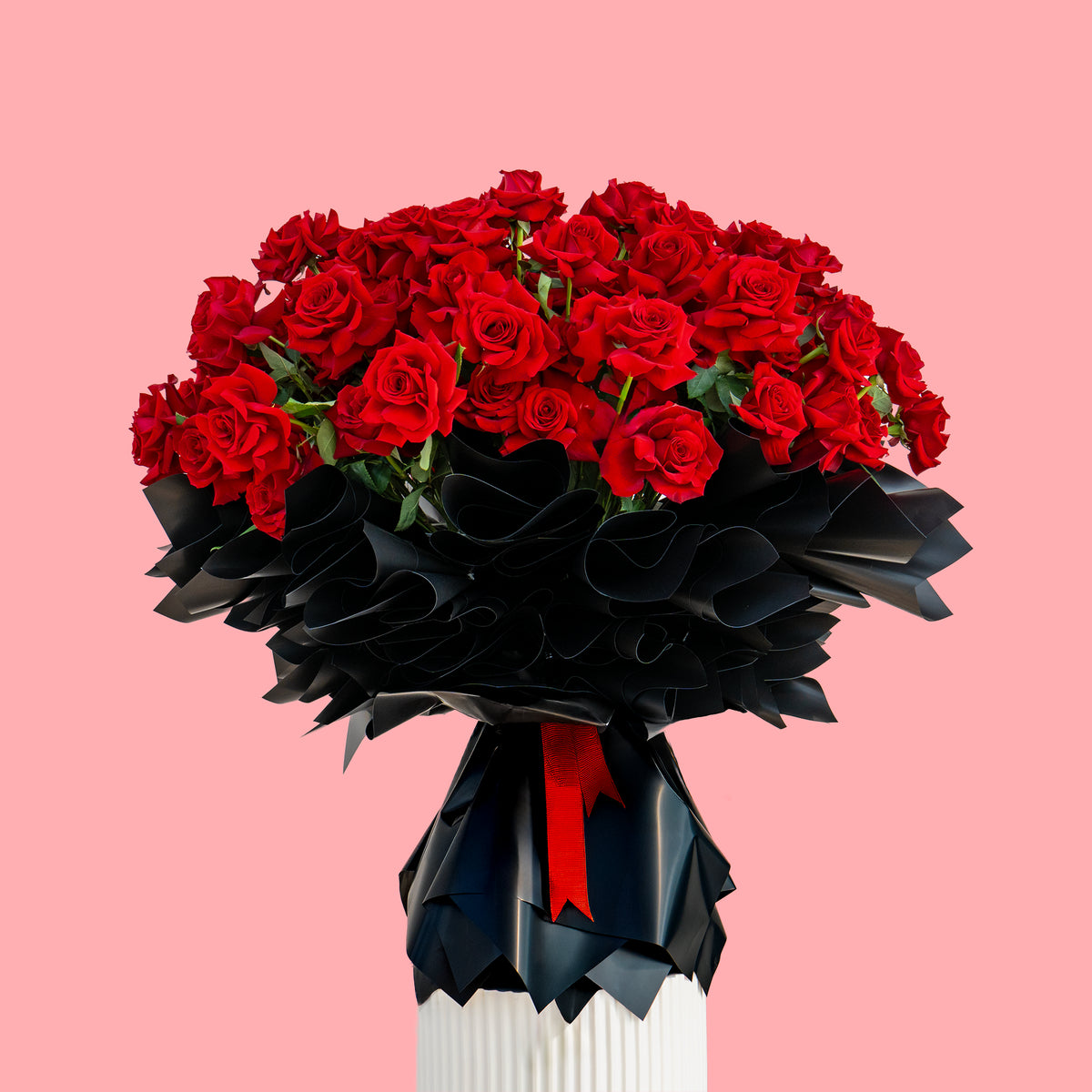 Bouquet of red roses in a black and white vase on a pink background