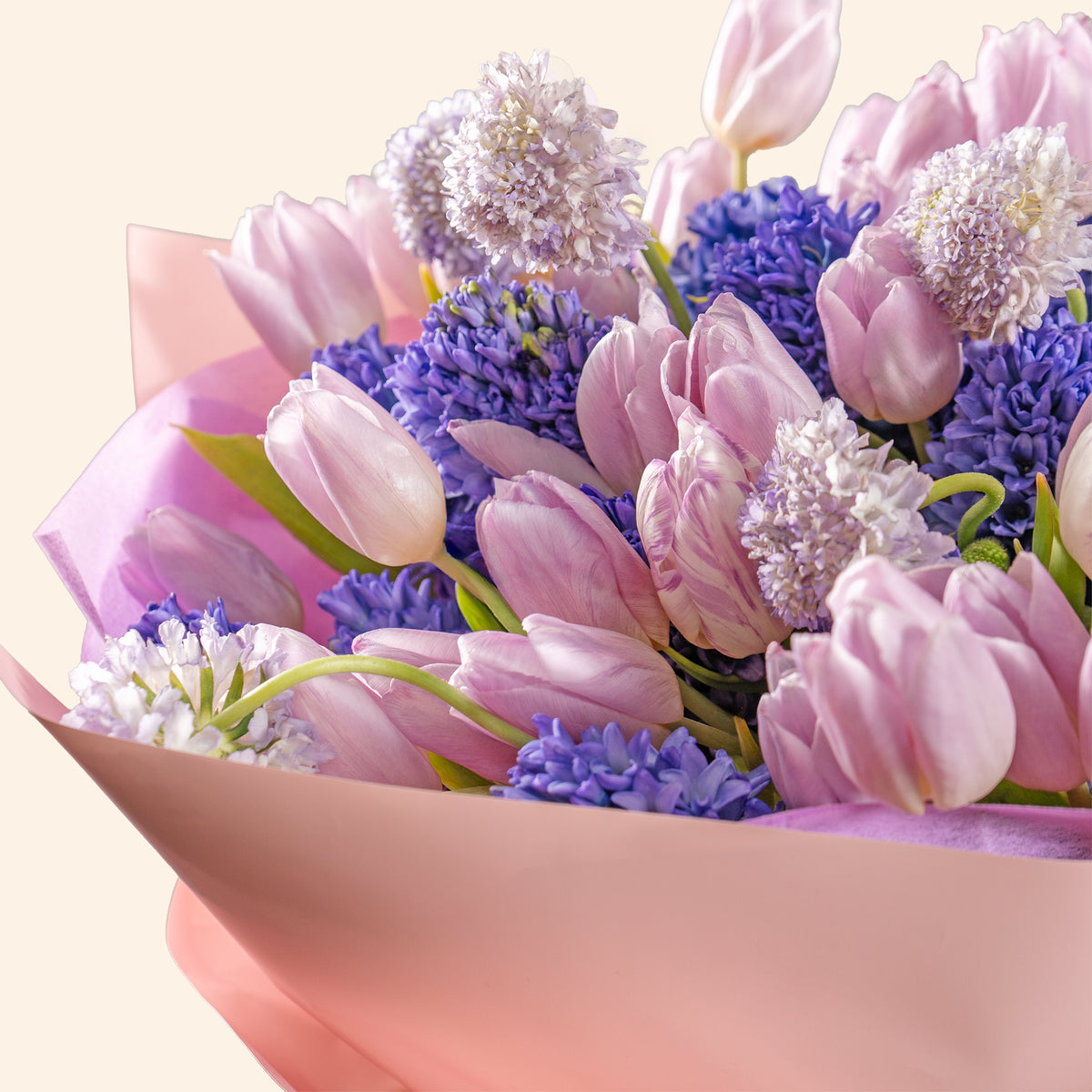 Bouquet of pink tulips and purple flowers in a clear vase on a light background