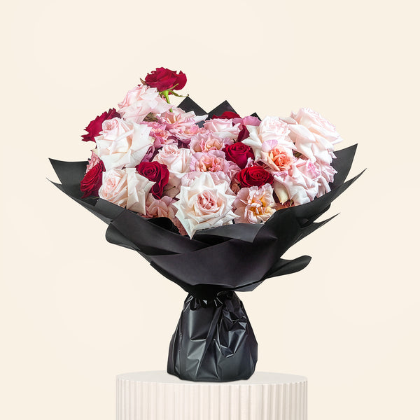 Bouquet of red and white flowers wrapped in black paper on a light gray background