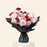 Bouquet of red and white flowers wrapped in black paper on a light gray background