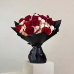 Bouquet of red and pink roses wrapped in black paper on a white pedestal against a light gray background