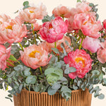 Bouquet of pink and peach flowers with greenery in a woven basket on a light background