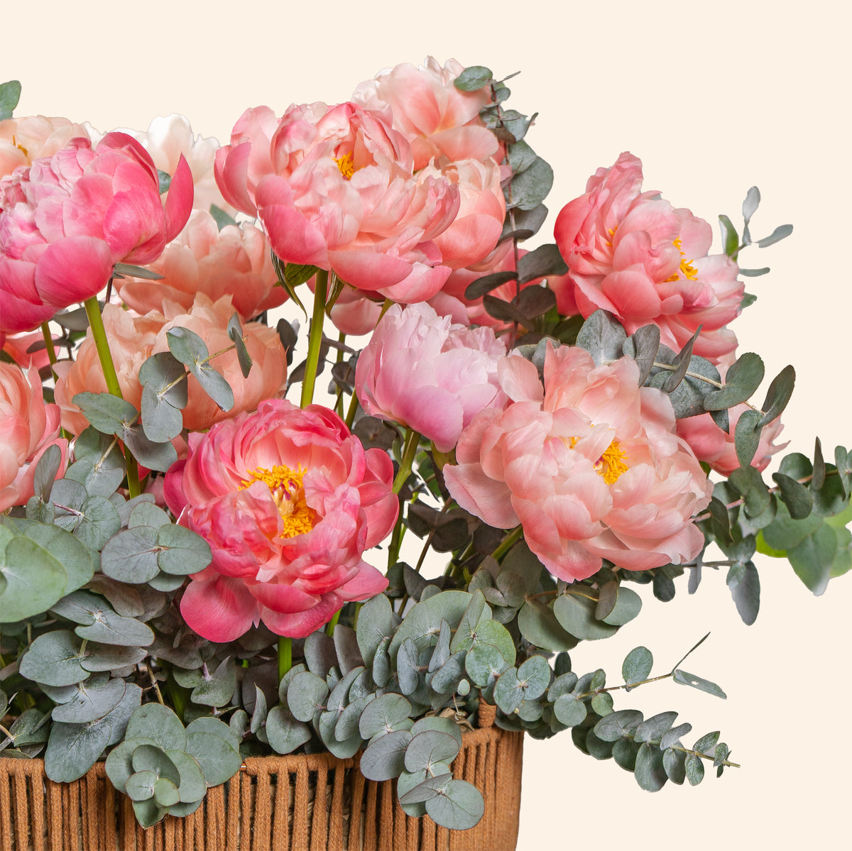 Bouquet of pink flowers with green leaves in a woven basket on a light background