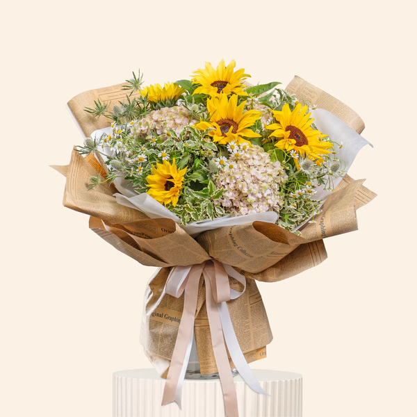 Bouquet of sunflowers and baby's breath wrapped in brown paper with a white ribbon on a light beige background.