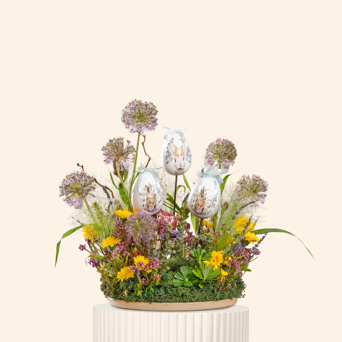 Decorative arrangement with flowers and Easter eggs on a white pedestal against a beige background