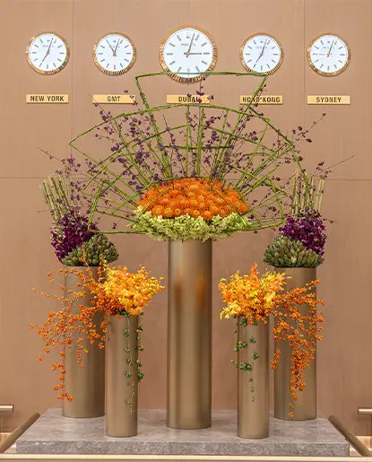 Floral arrangement with decorative clocks above on a beige wall.