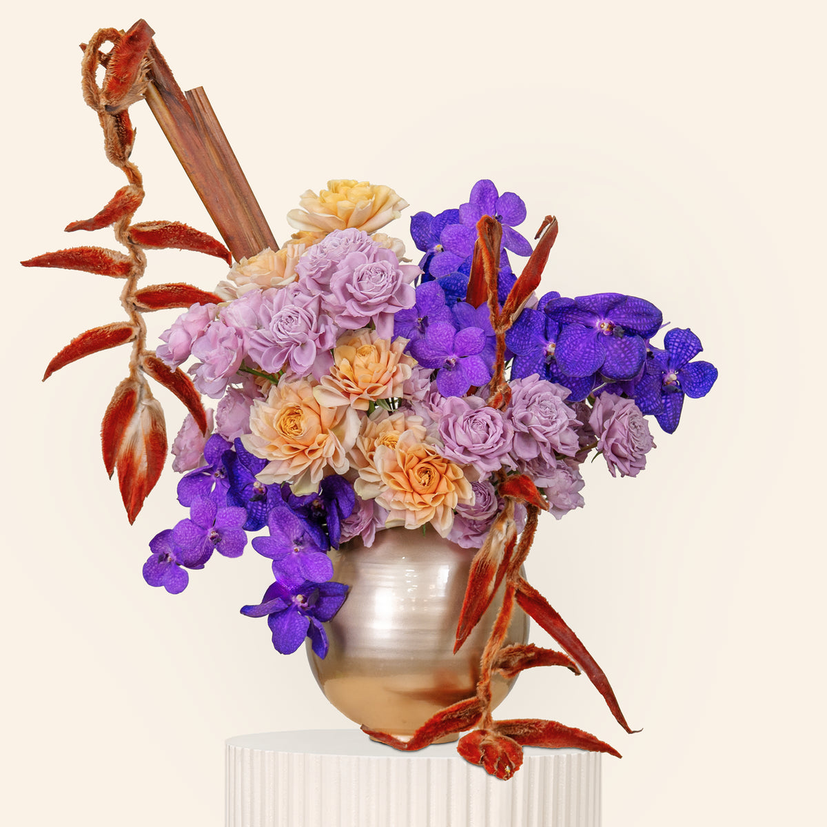 Colorful floral arrangement with purple and orange flowers in a metallic vase on a beige background