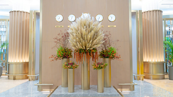 Decorative floral arrangement in a modern indoor setting with gold columns and clocks on the wall.
