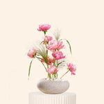 Decorative flower arrangement in a stone-like pot on a white pedestal against a light beige background