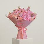Bouquet of pink flowers wrapped in pink paper on a light gray background