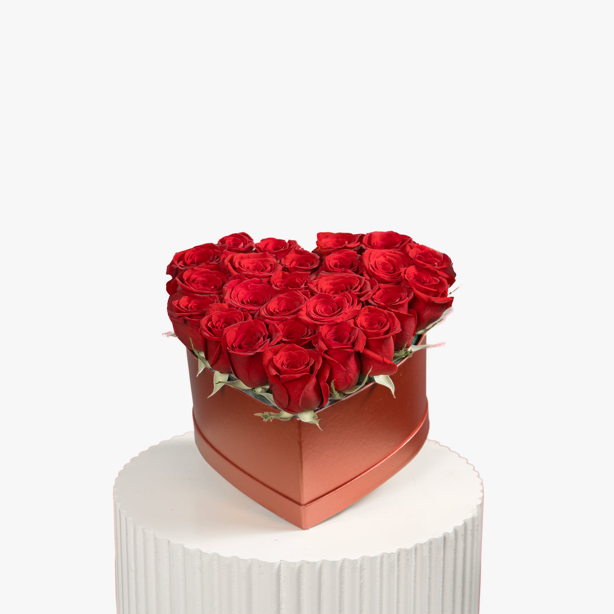 Heart-shaped box of red roses on a white pedestal with a white background