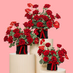 Bouquets of red roses with green leaves on white stands against a pink background