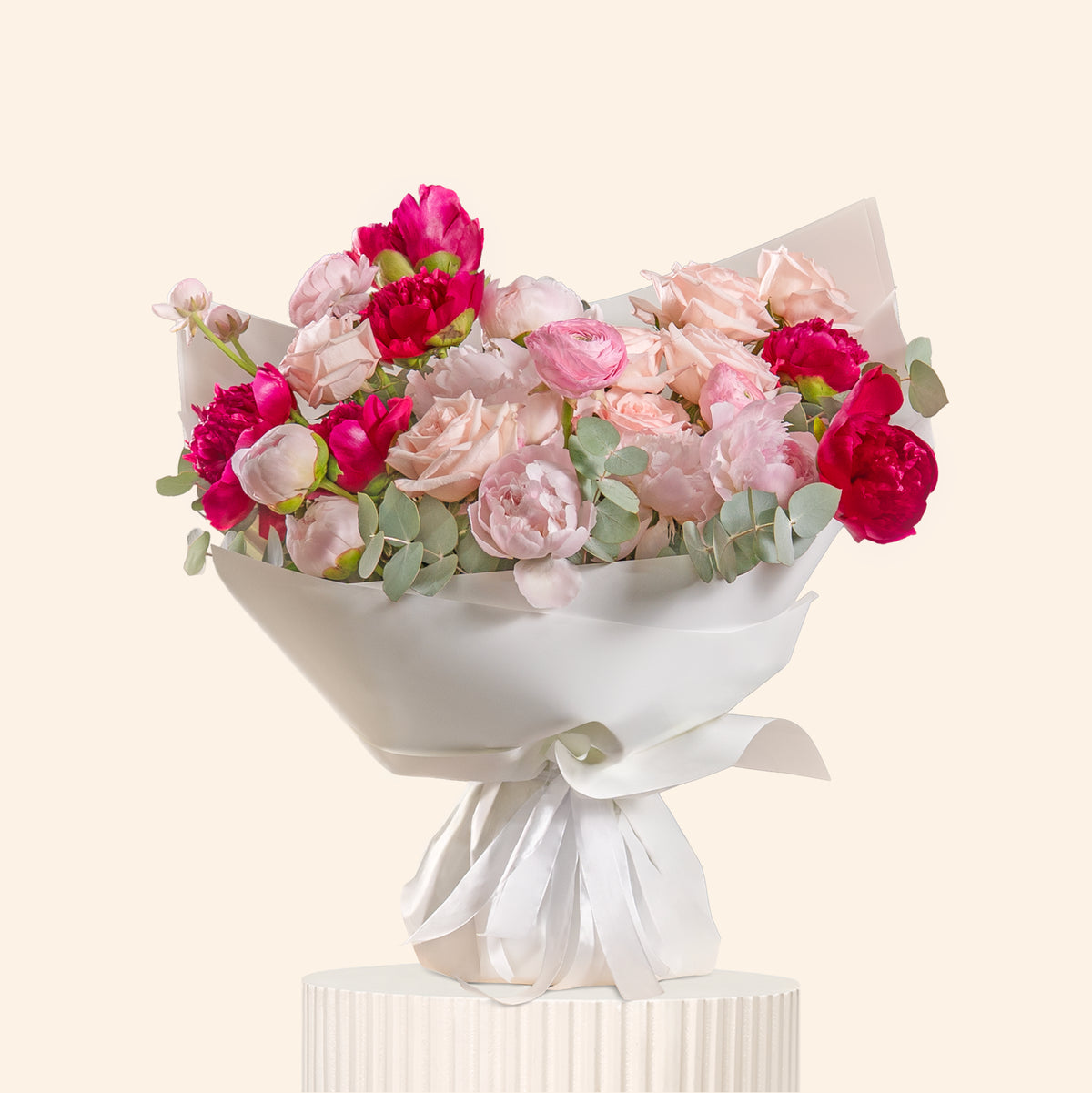 Bouquet of pink and red flowers wrapped in white paper on a light beige background