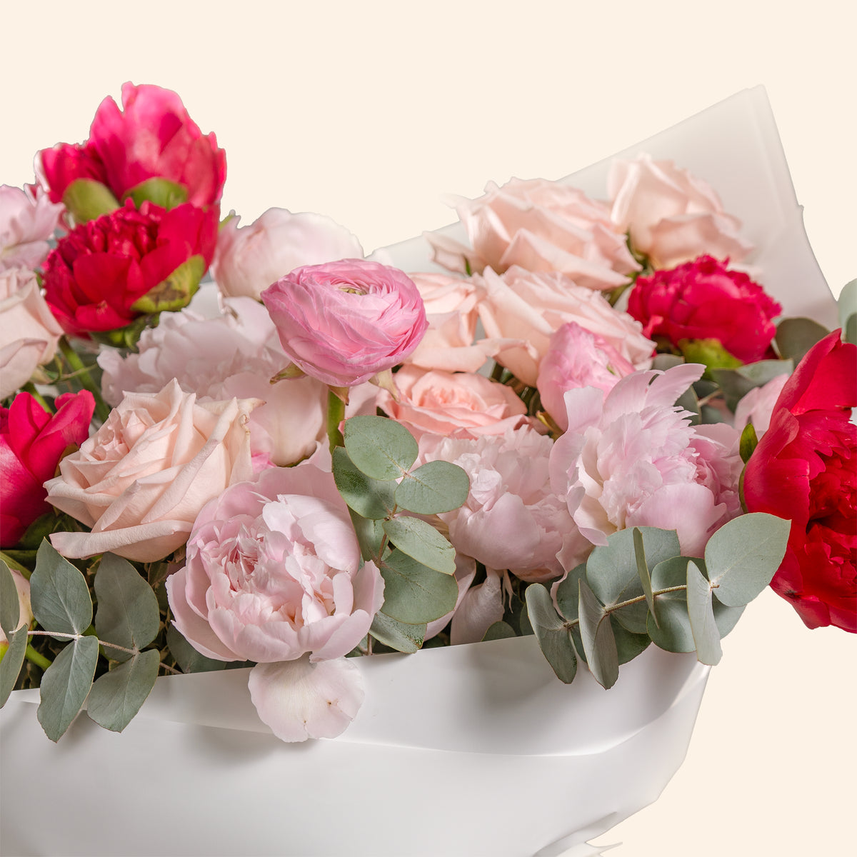 Bouquet of pink and red flowers with green leaves in a white container on a light background