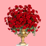 Bouquet of red roses in a gold urn on a pink background