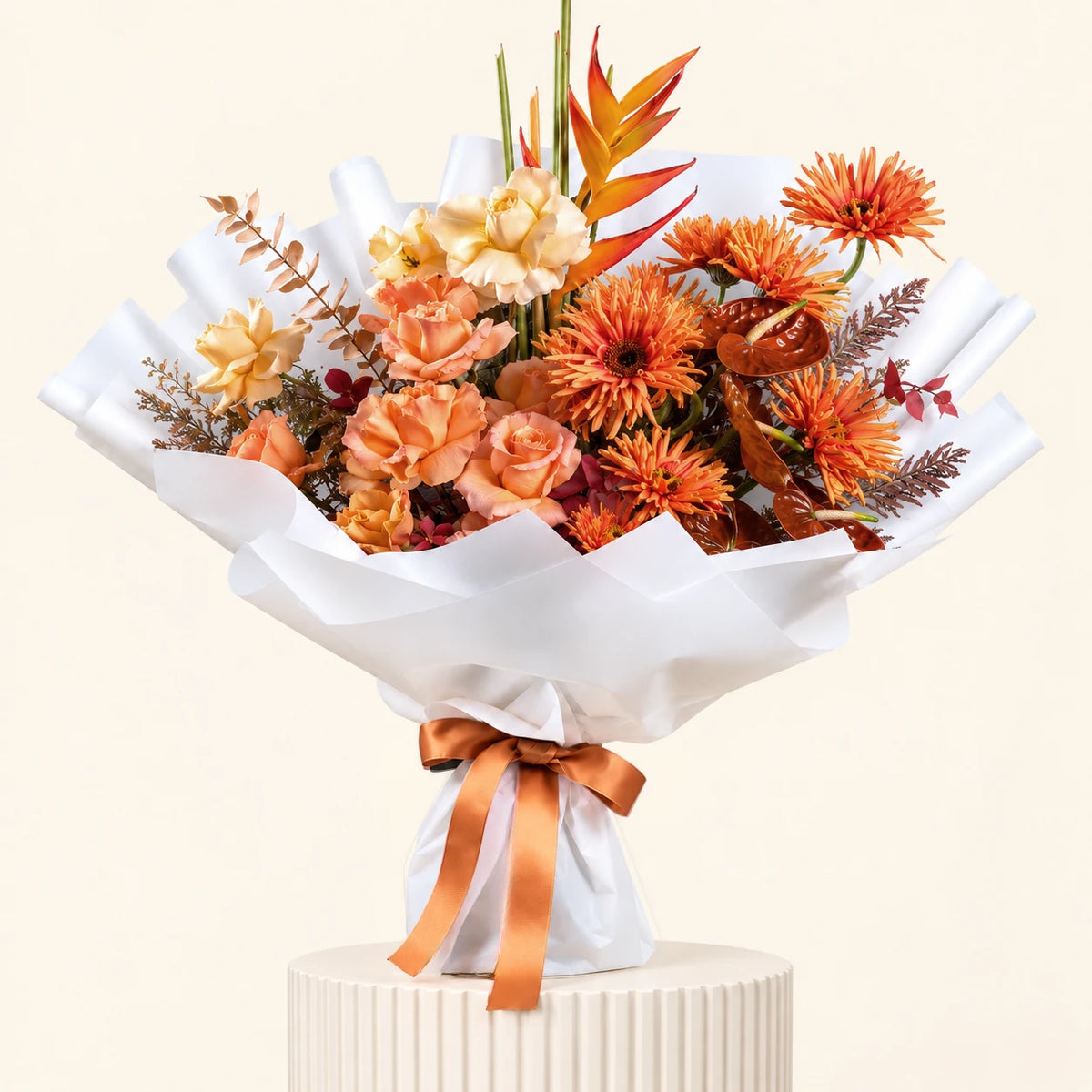 A floral arrangement bouquet with orange and peach flowers, wrapped in white paper with a peach ribbon, displayed on a white pedestal against a light beige background.