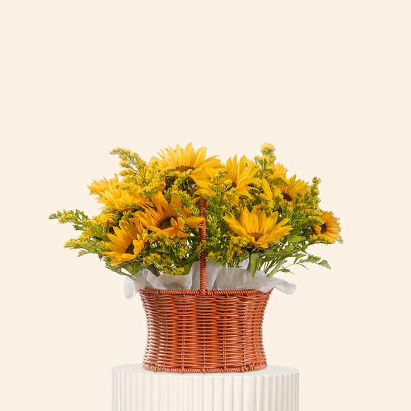 Bouquet of yellow flowers in a wicker basket on a white pedestal against a light beige background