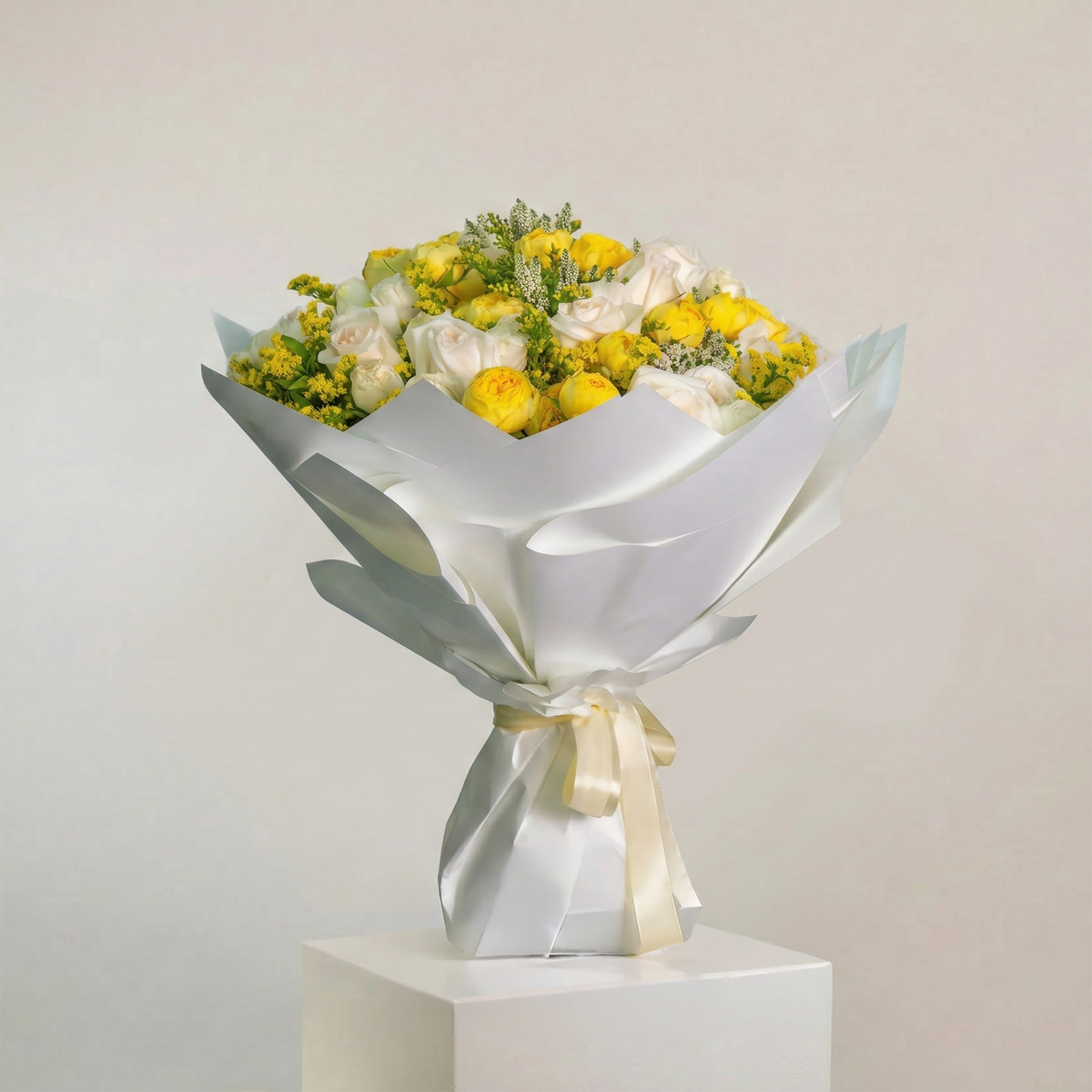Bouquet of yellow and white flowers wrapped in silver paper on a light gray background
