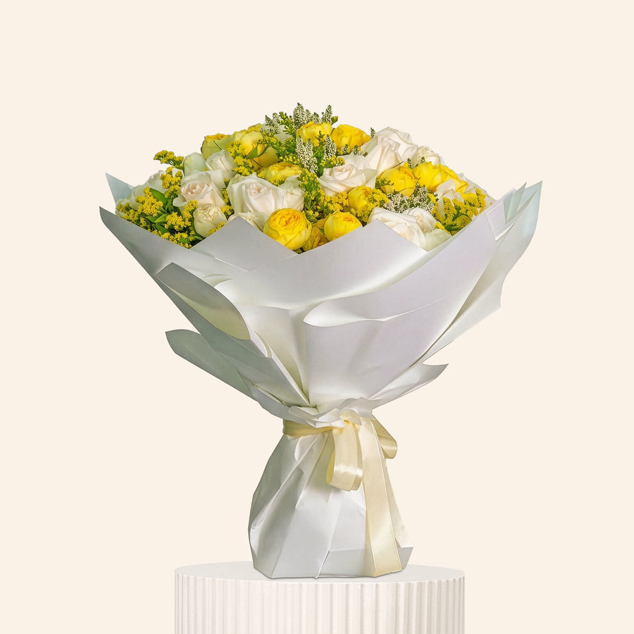 Bouquet of yellow and white flowers wrapped in silver paper on a light gray background