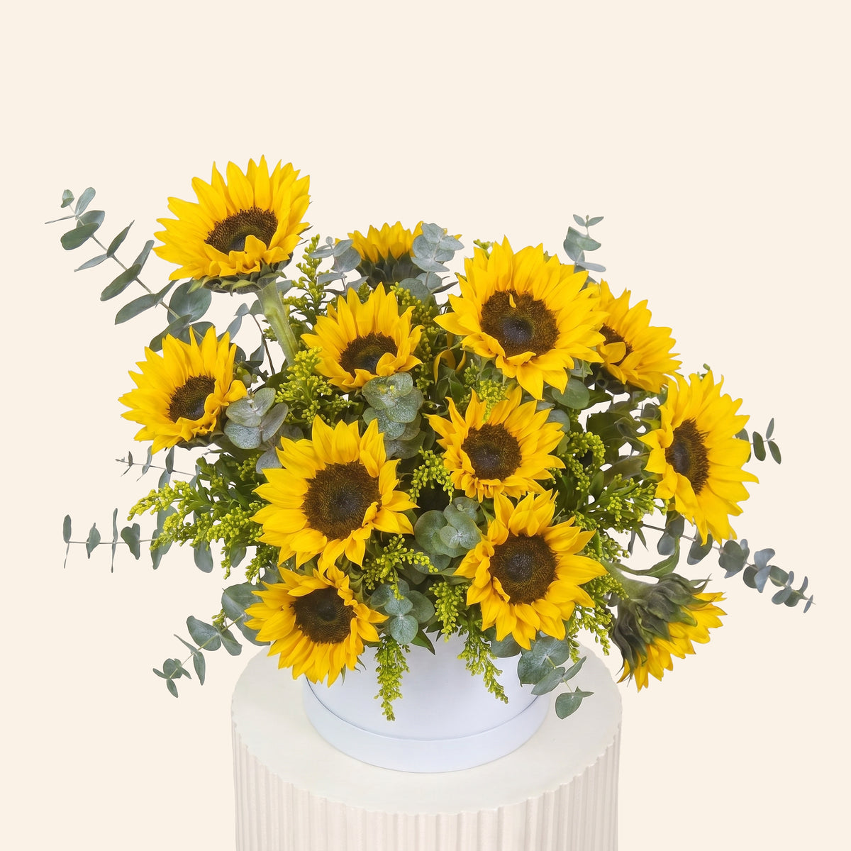 Bouquet of sunflowers with greenery on a white pedestal against a light beige background