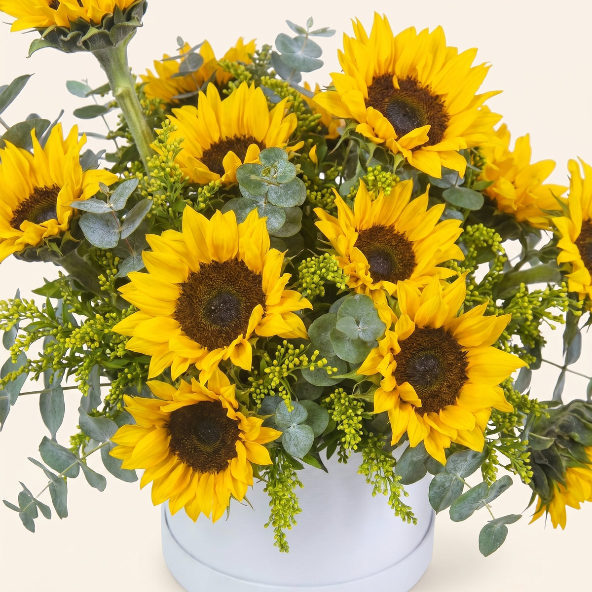 Bouquet of yellow sunflowers with greenery in a white container on a light background