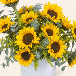 Bouquet of yellow sunflowers with greenery in a white container on a light background