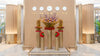 Decorative setup with floral arrangements in tall cylindrical vases against a beige wall with clock displays.
