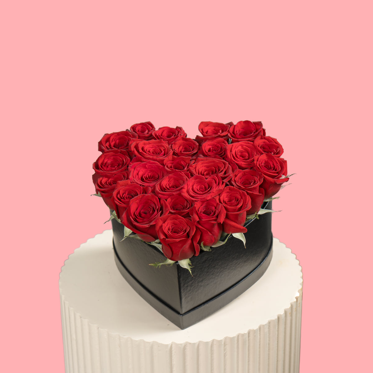 Heart-shaped box of red roses on a white pedestal with a pink background