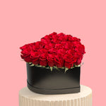Heart-shaped arrangement of red roses in a black box on a pink background