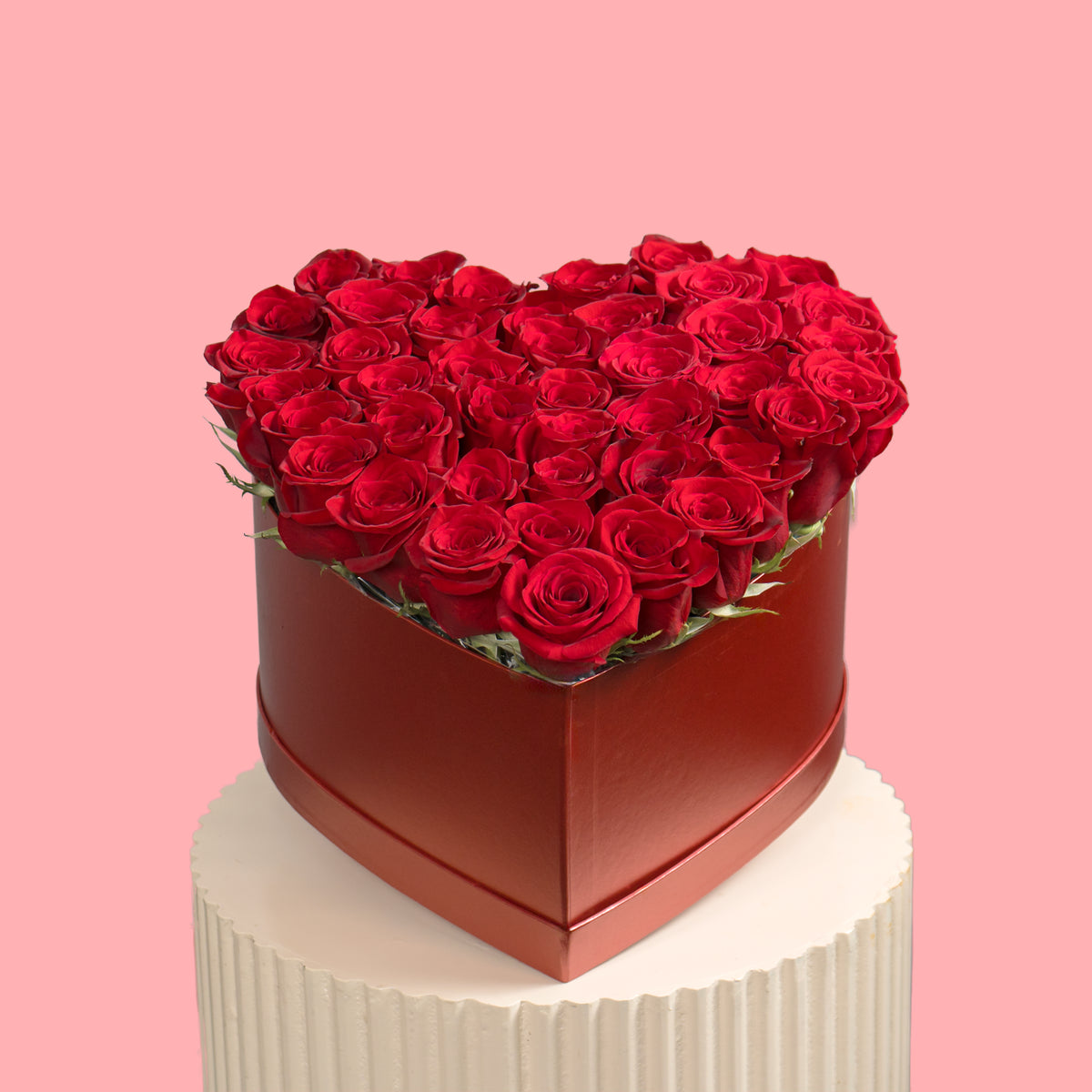 Heart-shaped box filled with red roses on a pink background